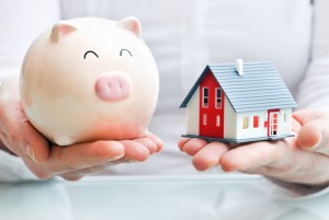 A person holding a piggy bank and a house