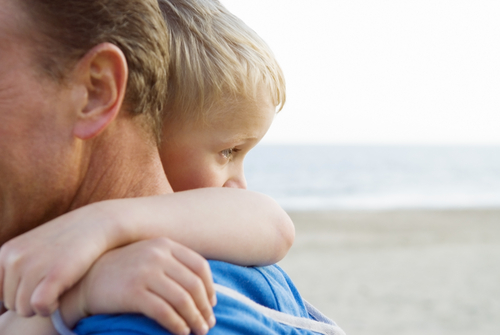 A man and his son are hugging on the beach.
