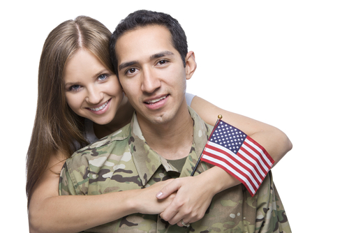 A man and woman hugging in uniform with an american flag.